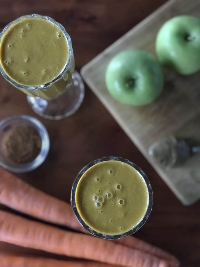 carrots, apples, coconut milk and more blended into a smoothie in a tall glass