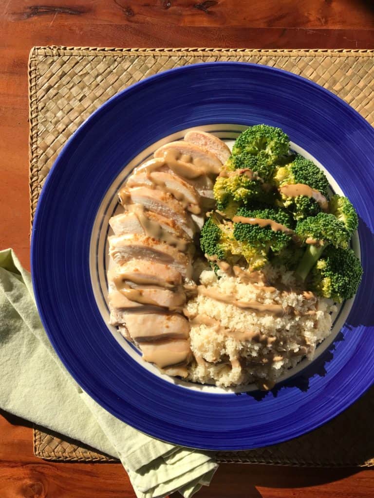 "Peanut" sauce drizzled over chicken, broccoli and cauliflower rice on a blue plate, straw placemat and green napkin