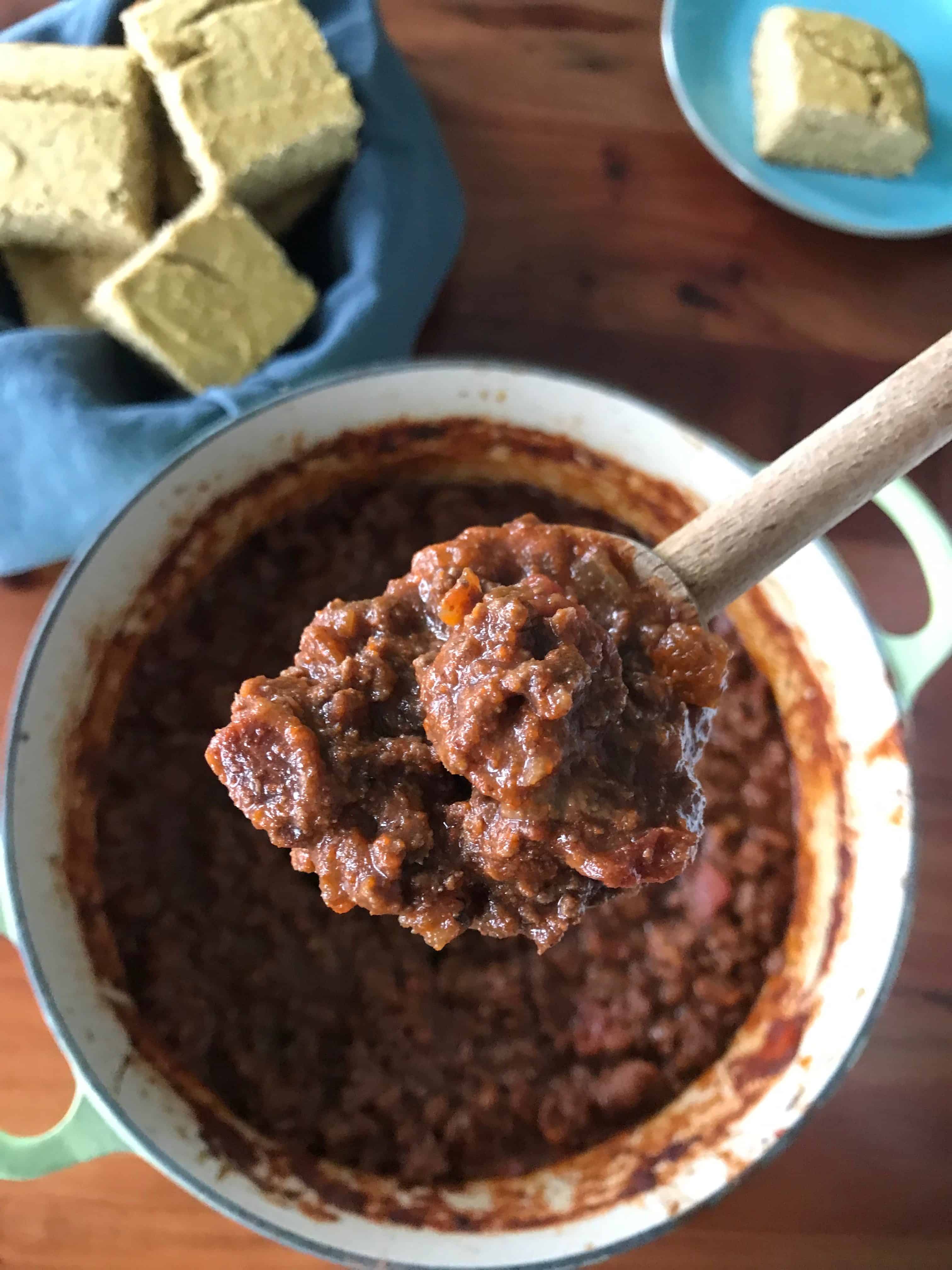 Smoky Bacon Chili on a spoon over a big pot with cornbread on the side