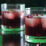 2 Pomegranate Old Fashioneds in rocks glasses on black marble surrounded by pomegranate arils
