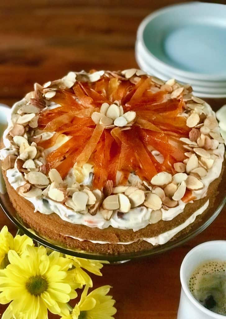 Cassata Cake on a glass cake stand on a wooden table surrounded by plates, napkins, forks and mugs of coffee