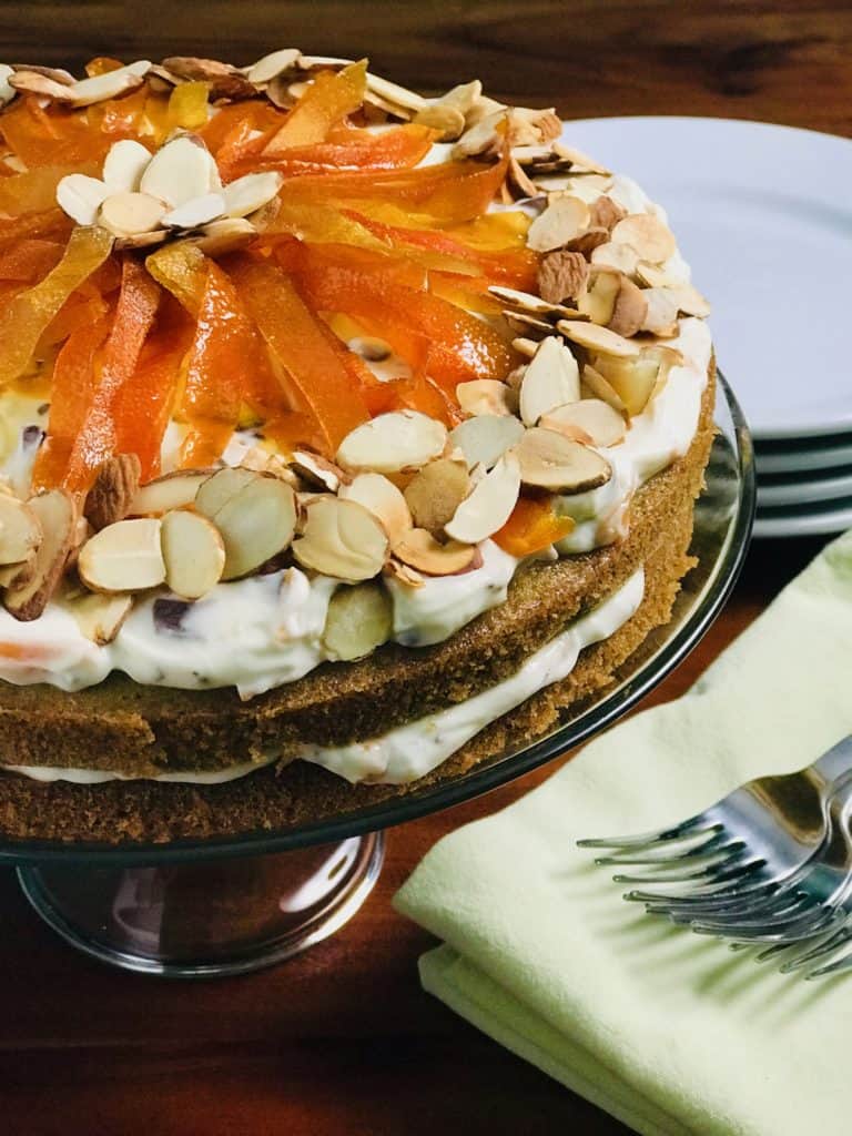 Cassata Cake on a glass cake stand on a wooden table surrounded by plates, napkins and forks