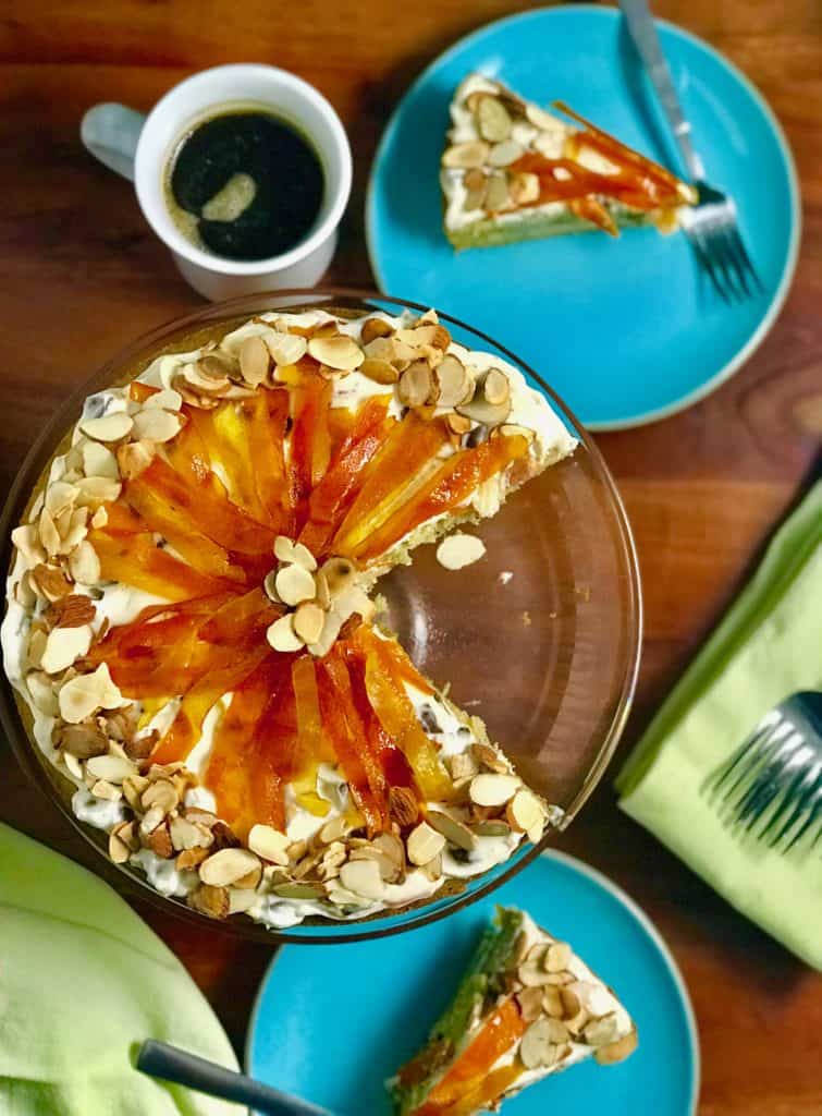 Cassata Cake on a glass cake stand on a wooden table surrounded by plates, napkins, forks and mugs of coffee