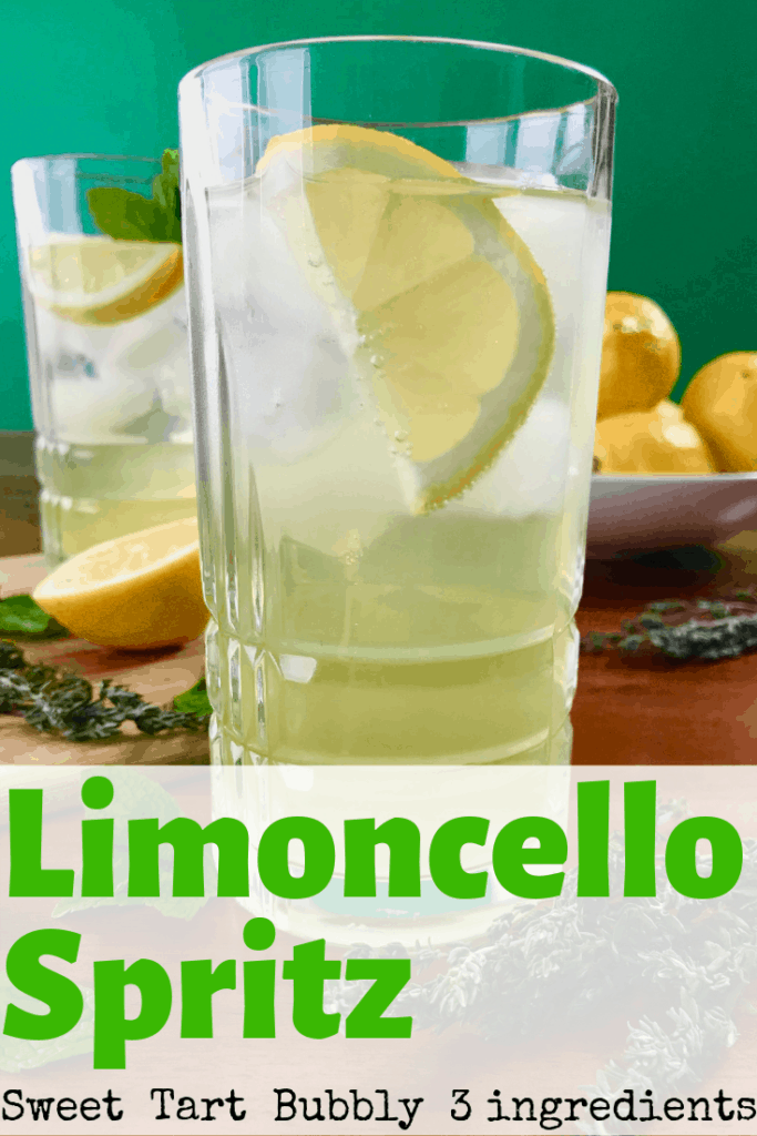 2 glasses of Limoncello Spritz on a wooden table surrounded by herbs and a bowl of lemons