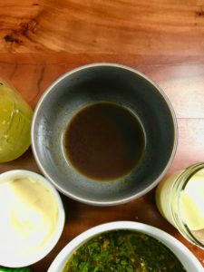 A close-up of Thai sauce in a gray bowl on a wooden table next to other condiments