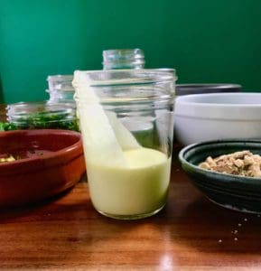 Lemon olive oil in a glass jar on a wooden table next to other condiments