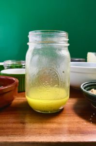 A vinaigrette in a glass jar next to other condiments on a wooden table