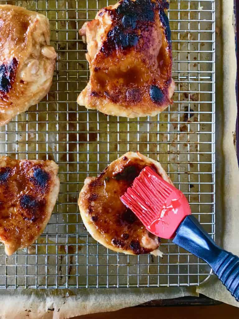 Healthy Teriyaki Chicken on a baking rack over parchment paper getting brushed with teriyaki sauce