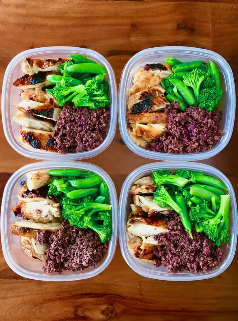 Healthy Teriyaki Chicken sliced and portioned into 4 plastic containers with purple sweet potato rice, broccoli and sugar snap peas, all on top of a wooden table