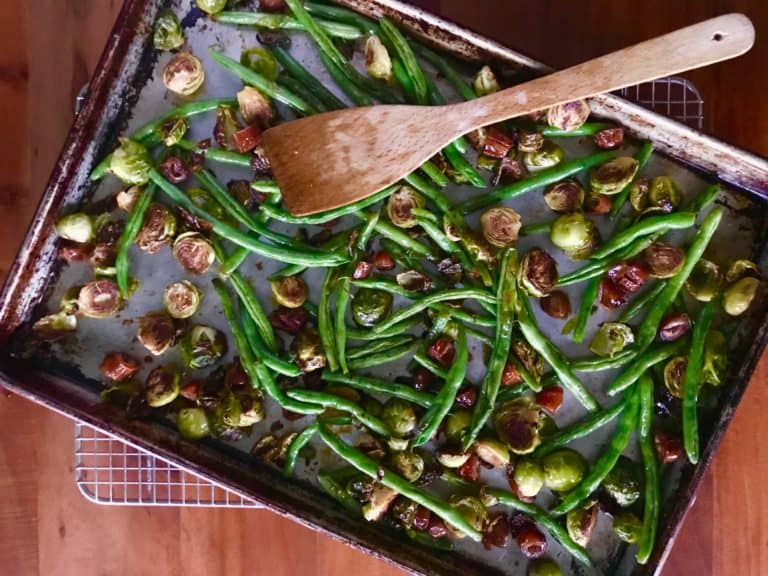 Roasted Green Beans and Brussel Sprouts with Dates and Balsamic Vinegar on a baking sheet on a wooden table