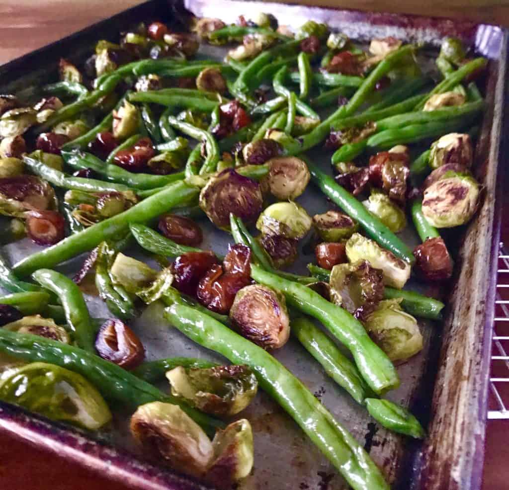 Roasted Green Beans and Brussel Sprouts with Dates and Balsamic Vinegar on a baking sheet on a wooden table