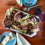 Grilled Italian Platter with Italian sausage, zucchini, romaine lettuce and raddichio with pistachios, dried cherries and olives on a white platter on a wooden table with Parmesan on the side