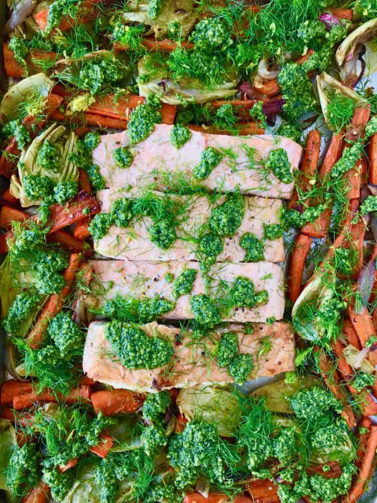 Sheet Pan Lemon Salmon with Pesto on a baking sheet with a fork cutting into the salmon, all on a wooden table