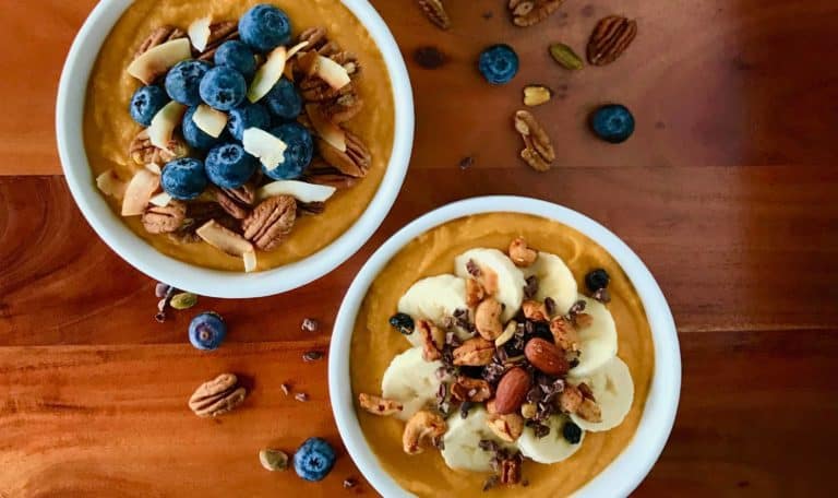 3 Sweet Potato Smoothie Bowls with different toppings in white bowls on a wooden table