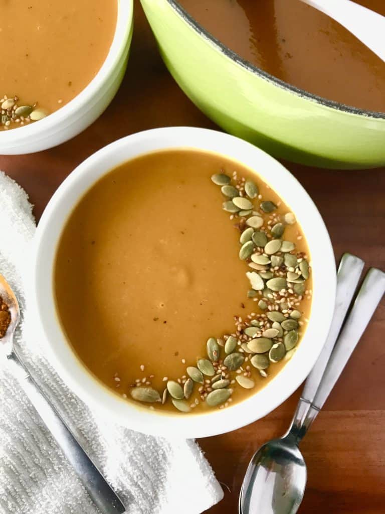 an image of curried sweet potato soup in a white bowl next to a green pot with more soup, all on a wooden table