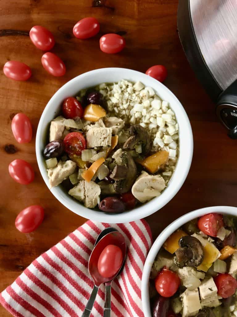 crockpot Italian chicken stew in the white bowls with cauliflower rice next to a red and white striped towel and cherry tomatoes, all on a wooden table