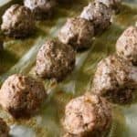 lots of Paleo meatballs on a parchment-lined baking sheet next to two white kitchen towels, all on a wooden table