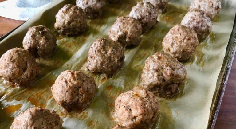 lots of Paleo meatballs on a parchment-lined baking sheet next to two white kitchen towels, all on a wooden table
