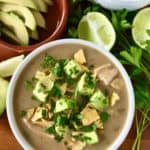 the best white chicken chili in white bowls on wooden tables surrounded by limes, avocado and parsley