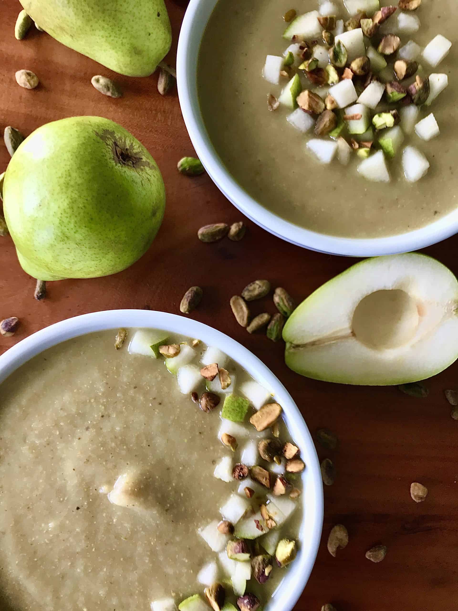 Healthy, creamy parsnip soup with pears and pistachios in white bowls on a wooden table