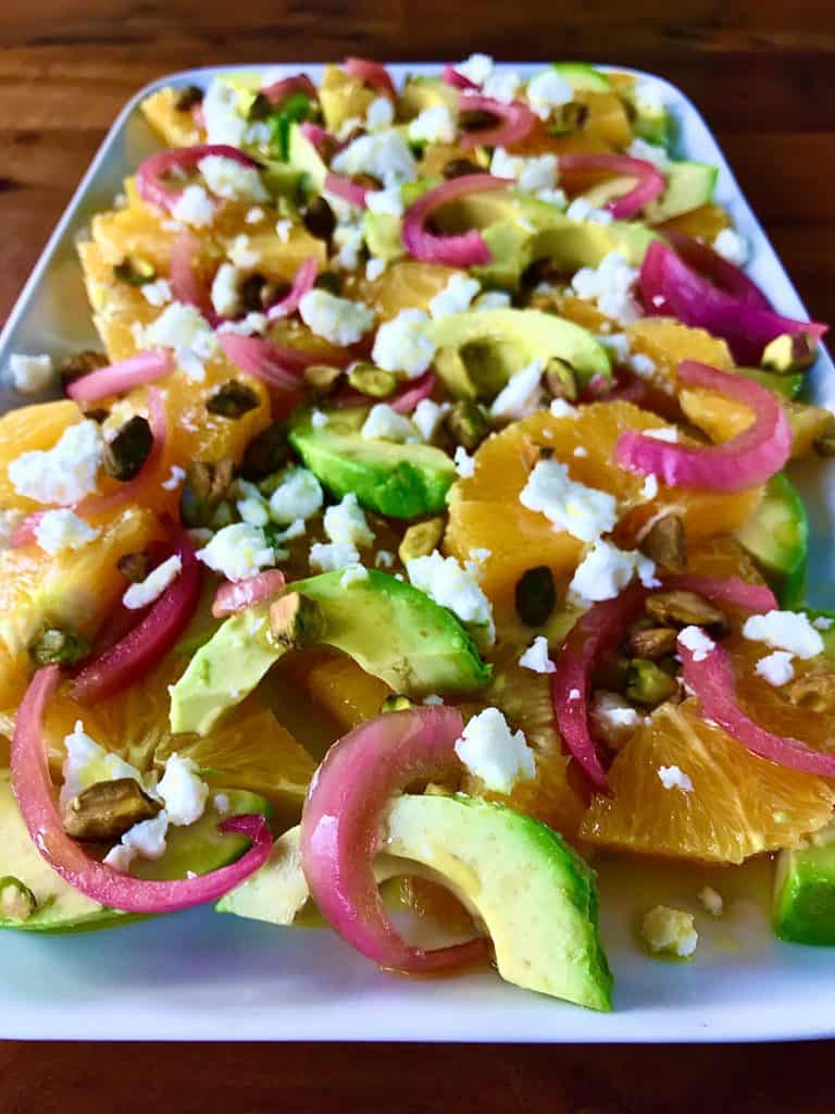 citrus, avocado, onion, feta and pistachios on a white platter on a wooden table