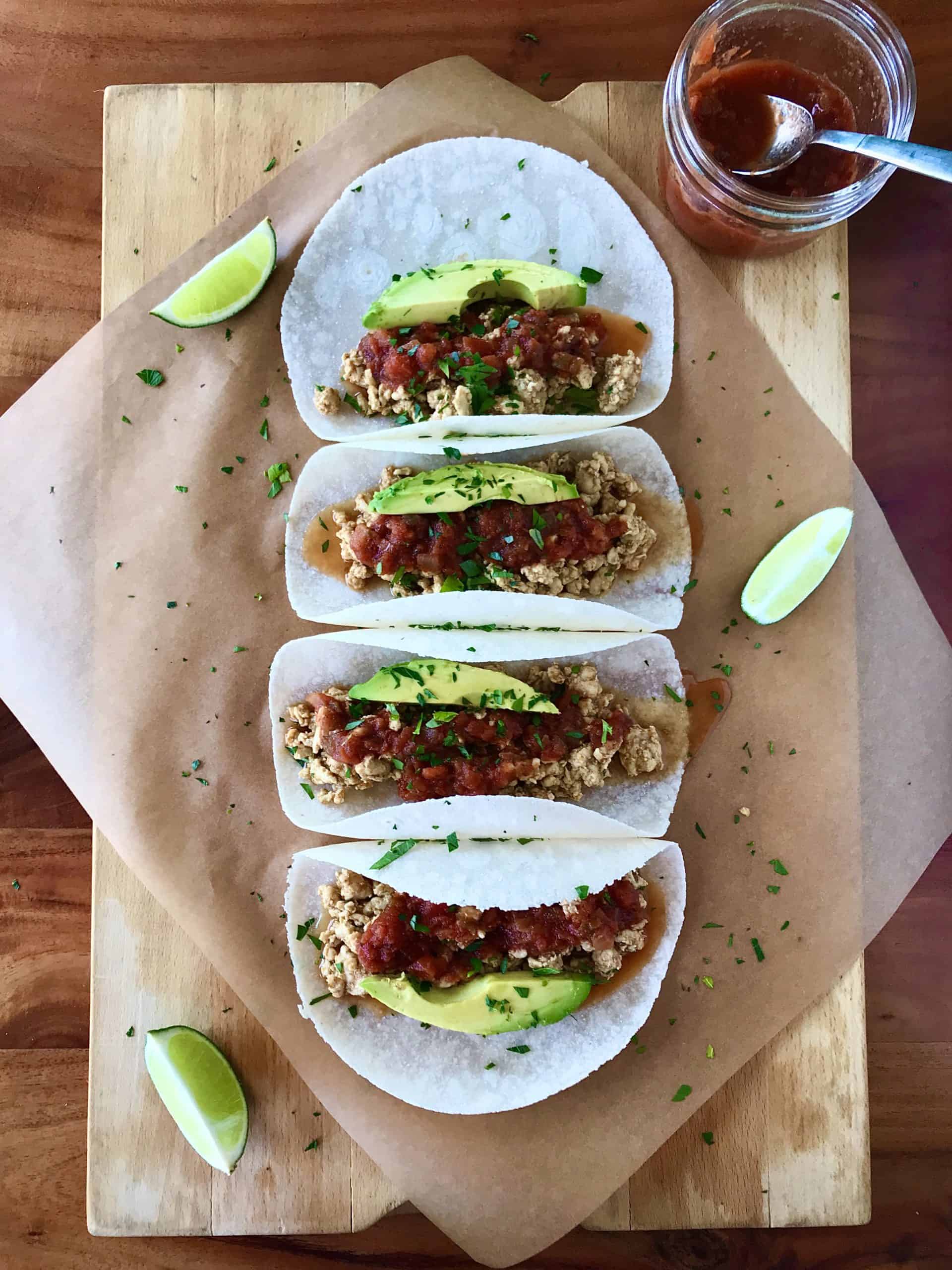ground chicken, salsa and avocado slices in tortillas on a wooden board on a wooden table
