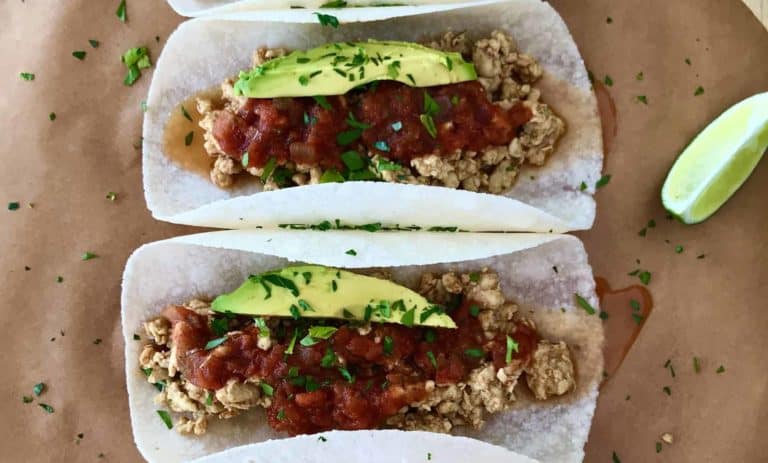 4 tacos with ground chicken, salsa and avocado on parchment paper on a wooden board
