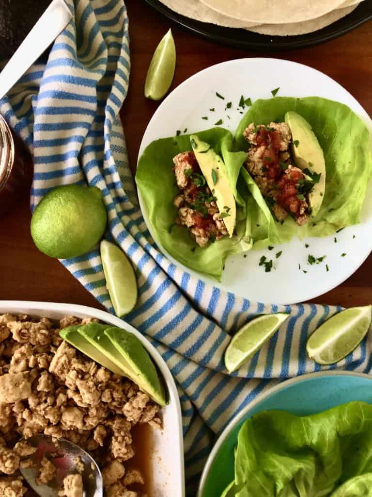chicken taco lettuce wraps on a table with ground chicken with taco seasoning, lettuce and a lime wedge