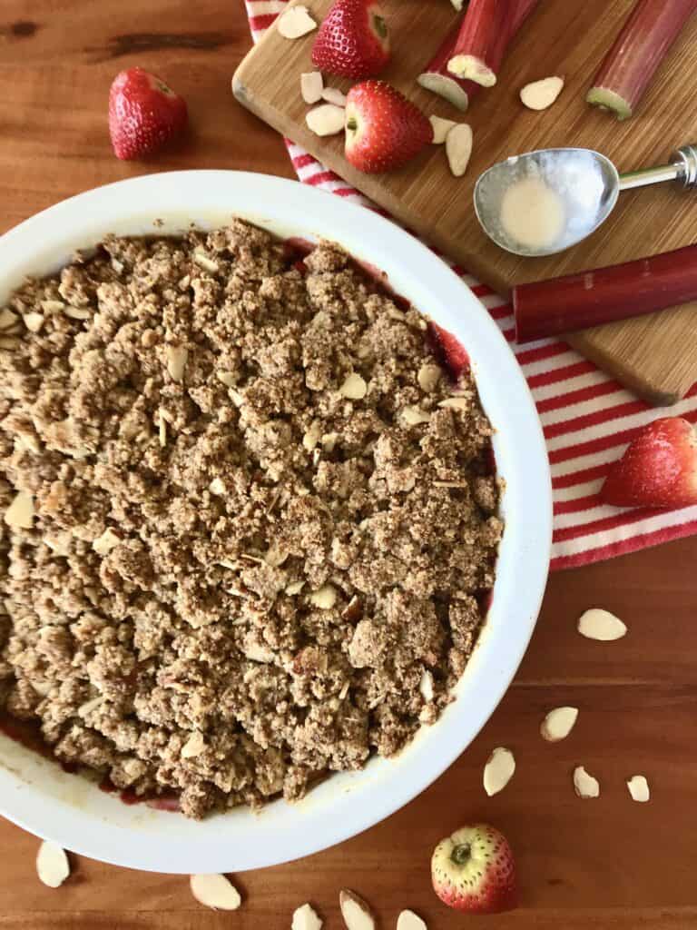 Strawberry rhubarb crisp that's paleo and gluten-free in a baking dish surrounded by strawberries, rhubarb and sliced almonds