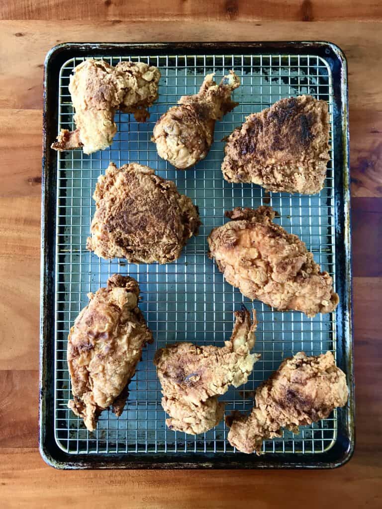 Gluten-free and dairy-free fried chicken on a cooling rack on a baking sheet, all on a wooden table