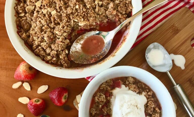Paleo strawberry rhubarb crisp in a baking dish with a spoon and in a bowl topped with ice cream