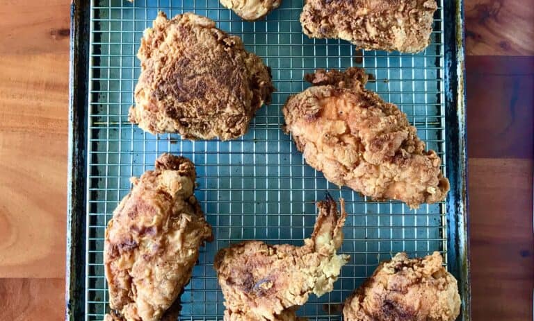 Cassava flour fried chicken on a cooling rack on a baking sheet, all on wooden table