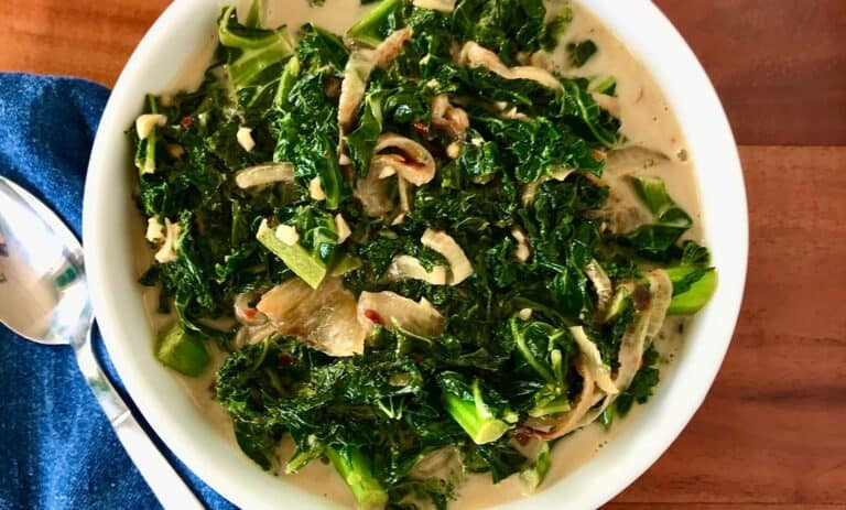 vegan creamed kale in a white bowl next to a denim towel and spoon on a wooden table