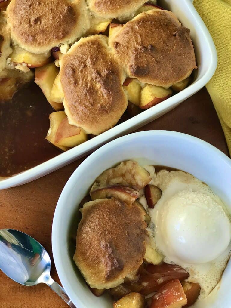 dairy free peach cobbler in a white baking dish and white bowl with ice cream