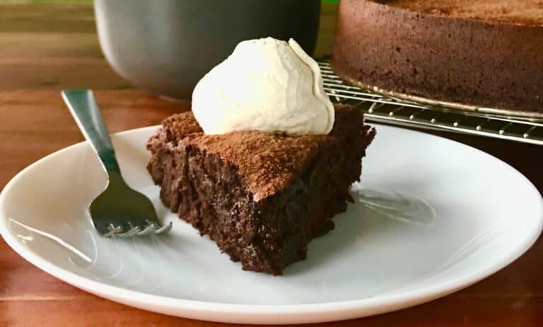 flourless chocolate cake with espresso powder on a white plate, topped with boozy whipped cream