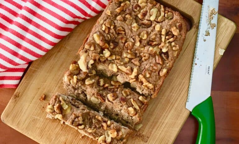 gluten-free apple bread on a cutting board with a knife and towel, all on a wooden table
