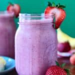 strawberry smoothie with bananas, yogurt and milk in a glass mason jar surrounded by strawberries and a red striped towel