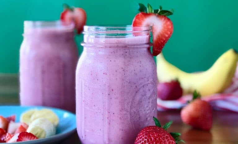 strawberry smoothie with bananas, yogurt and milk in a glass mason jar surrounded by strawberries and a red striped towel