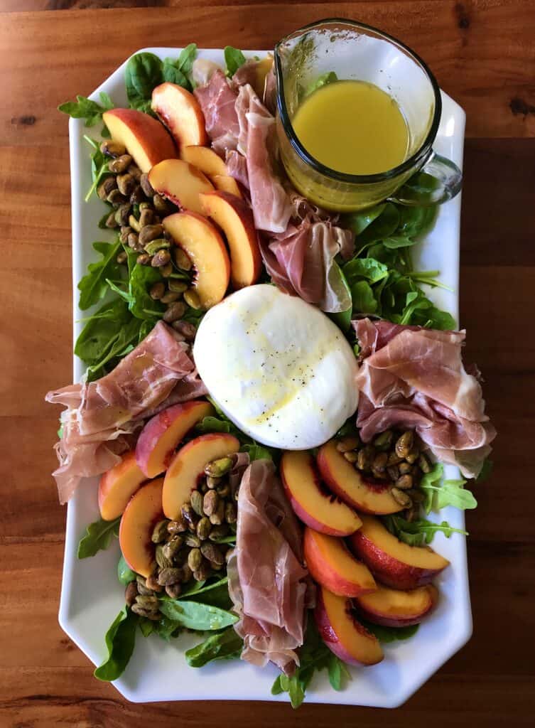 peach arugula salad with prosciutto and burrata on a white platter on a wooden table