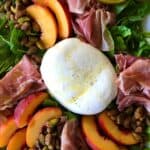 prosciutto salad with burrata and peaches on a white platter on a wooden table
