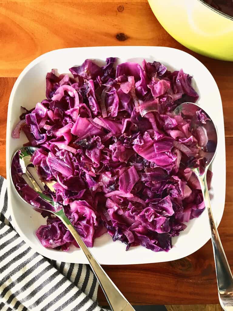 braised red cabbage and onions on a white platter on a wooden table