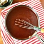 healthy bbq sauce in a pot on top of a red striped towel with a spoon above it holding some of the sauce