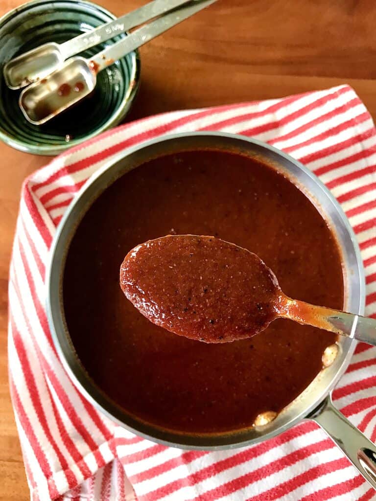 healthy bbq sauce in a pot on a red striped towel with a spoon holding the sauce above it