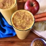 carrot apple coconut milk smoothie in a glass surrounded by apples, carrots and a bowl of cinnamon