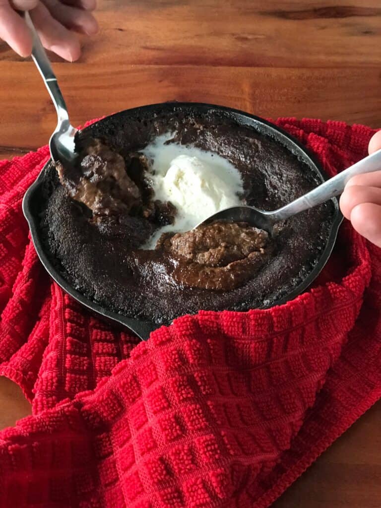 two spoons digging into a vegan cast iron pan cake with vanilla ice cream