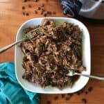 espresso pulled pork in a white dish on a wooden table next to a slow cooker