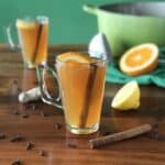 mulled cider in a glass on a wooden table with cloves, cinnamon sticks and ginger