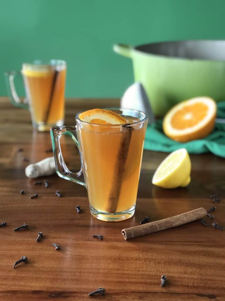 mulled cider in a glass on a wooden table with cloves, cinnamon sticks and ginger