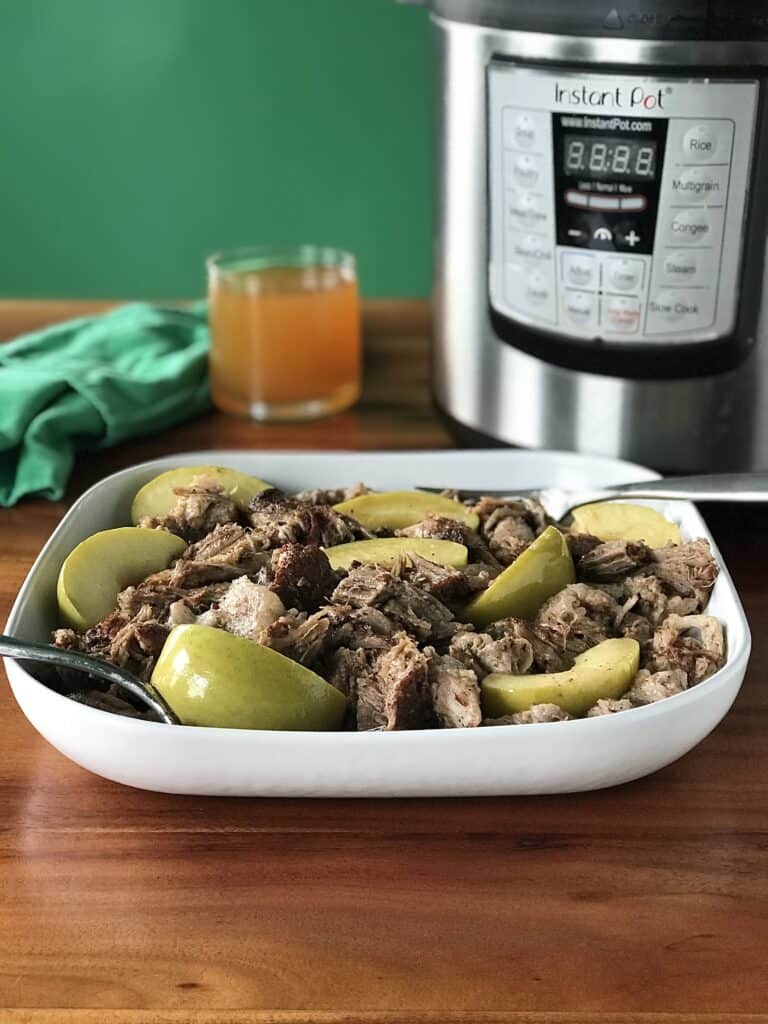 paleo pulled pork cooked with apples and apple cider in a white dish with 2 forks next to an Instant Pot