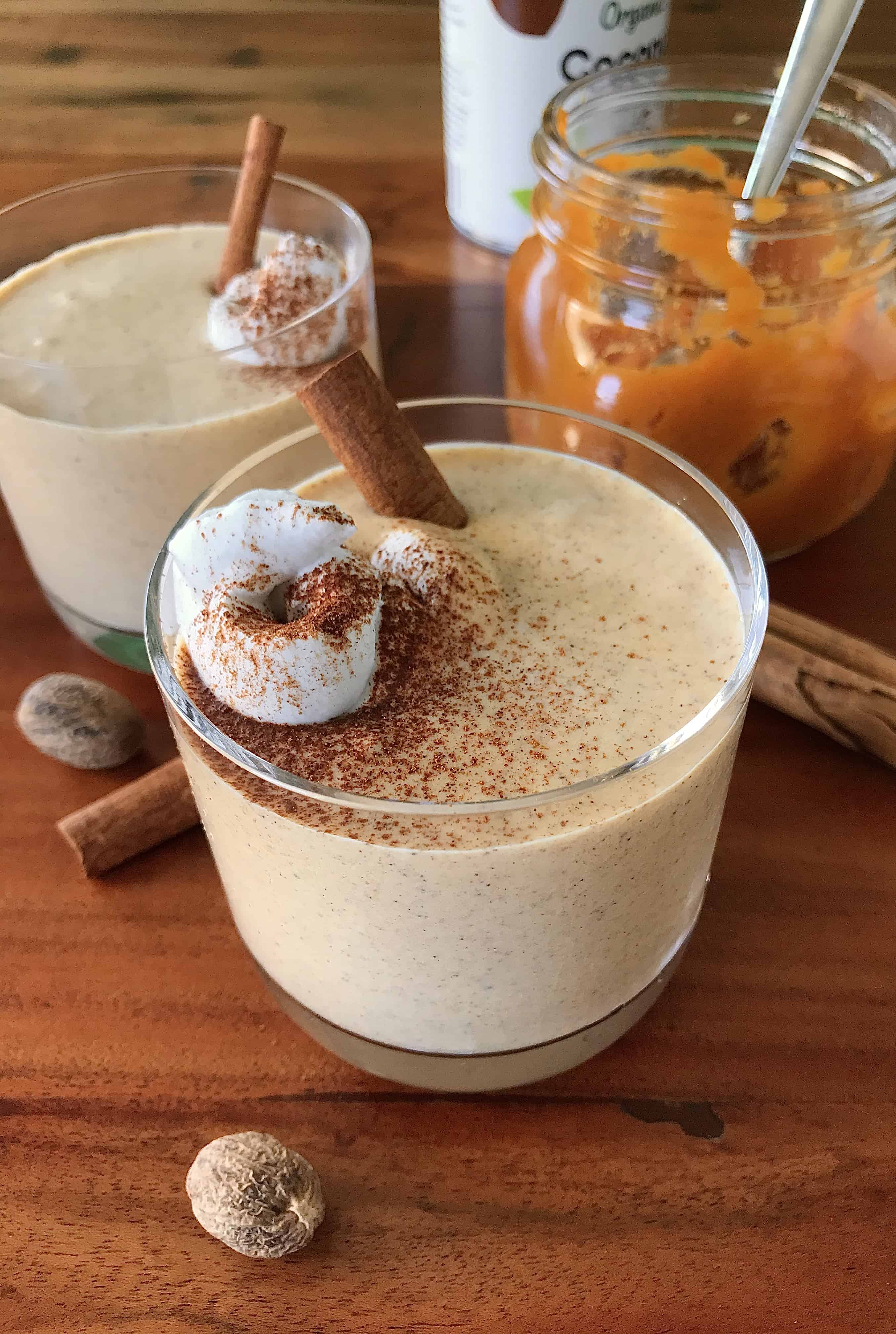 a dairy-free pumpkin smoothie in glasses next to a glass of pumpkin puree and cinnamon sticks